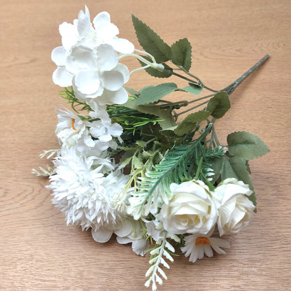 An artificial floral bouquet with Ivory faux flowers and green leaves, arranged on a light wood surface.