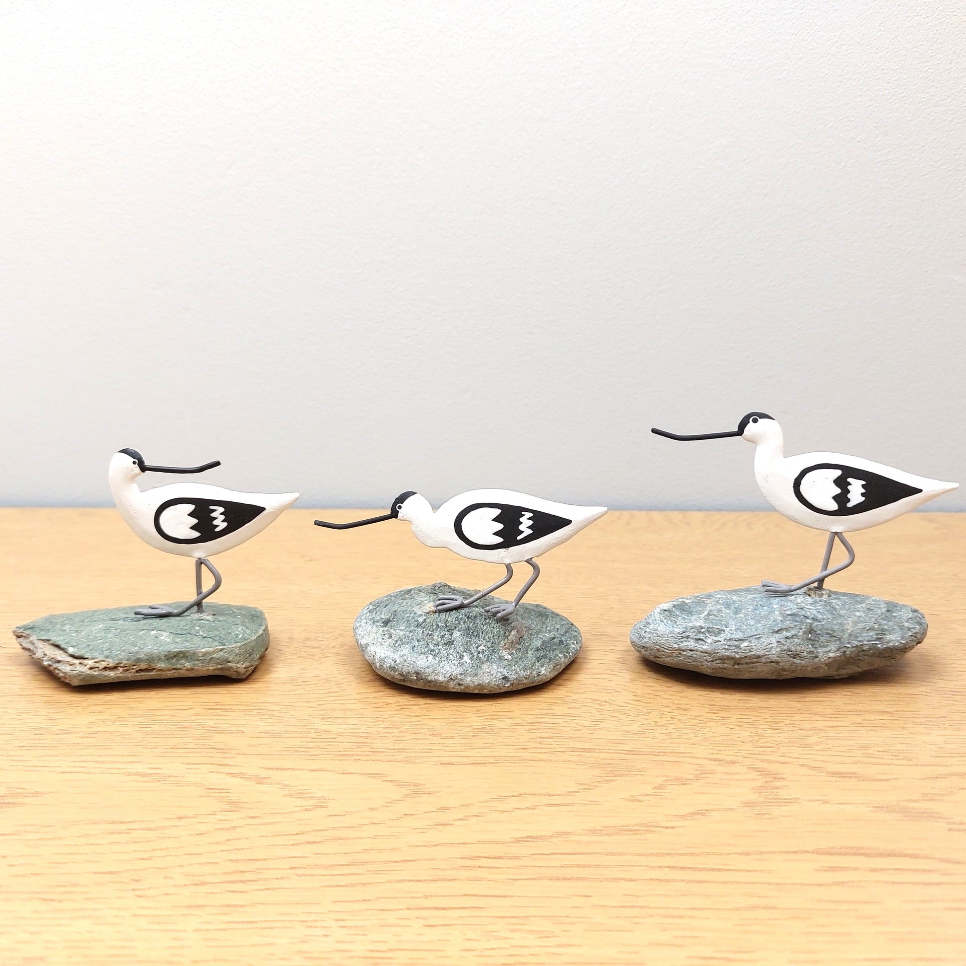 Three bird-shaped figurines on stone bases on a wooden surface with a light gray background