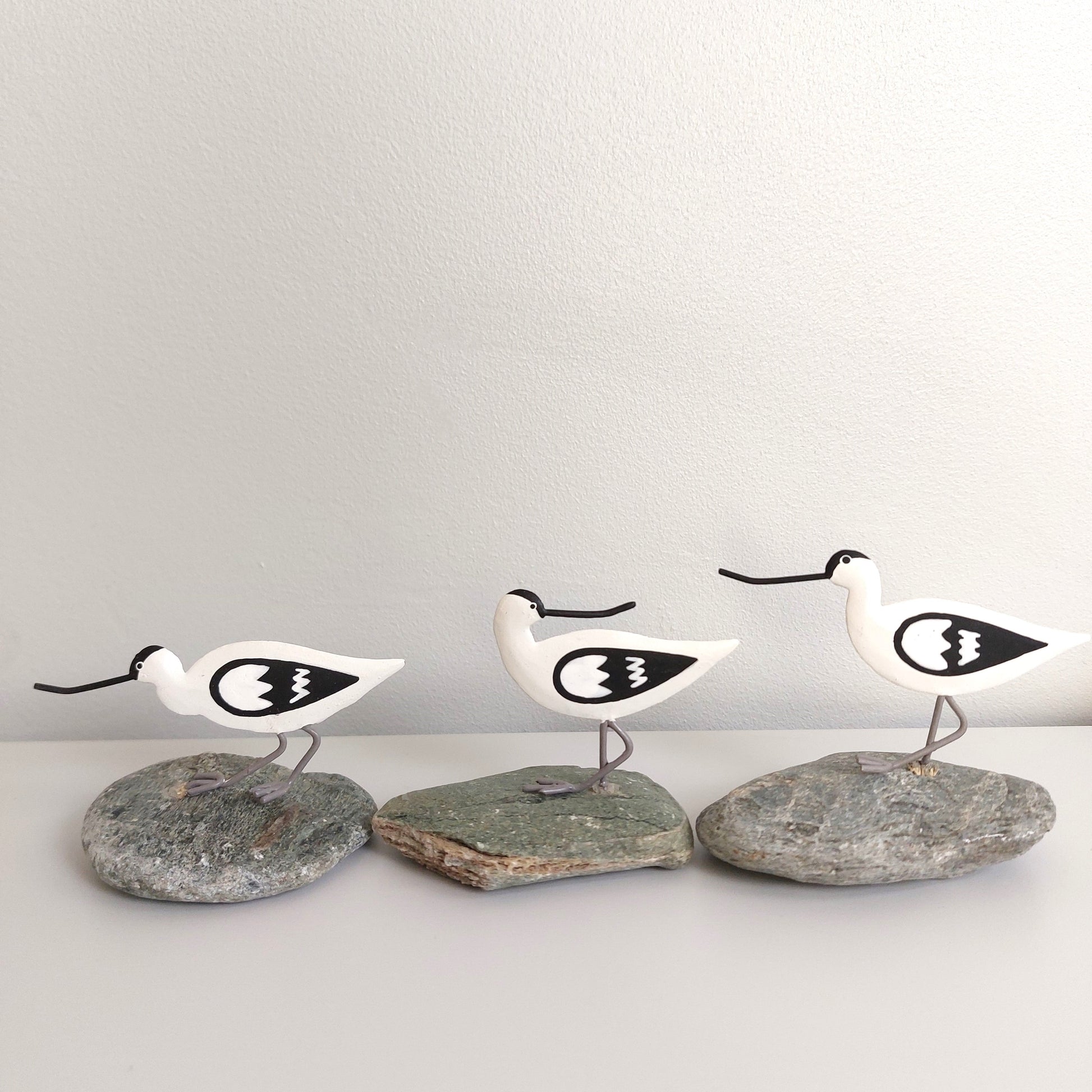Three white bird figurines with black details on gray stones against a light gray background