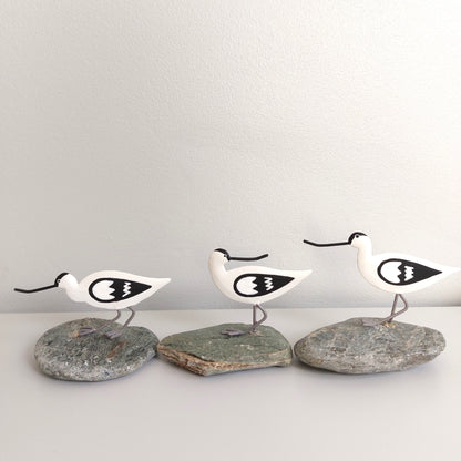 Three white bird figurines with black details on gray stones against a light gray background