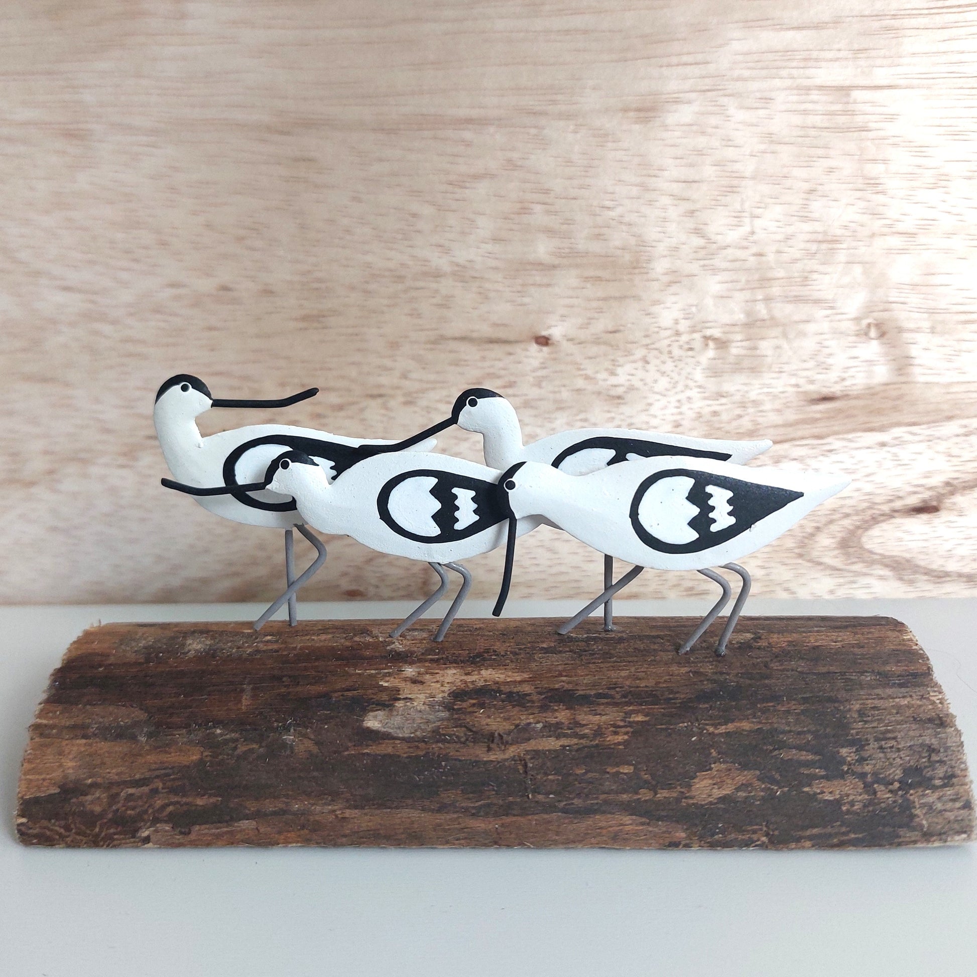Decorative metal sculpture of four white avocet birds with black patterns on a wooden base against a wooden background