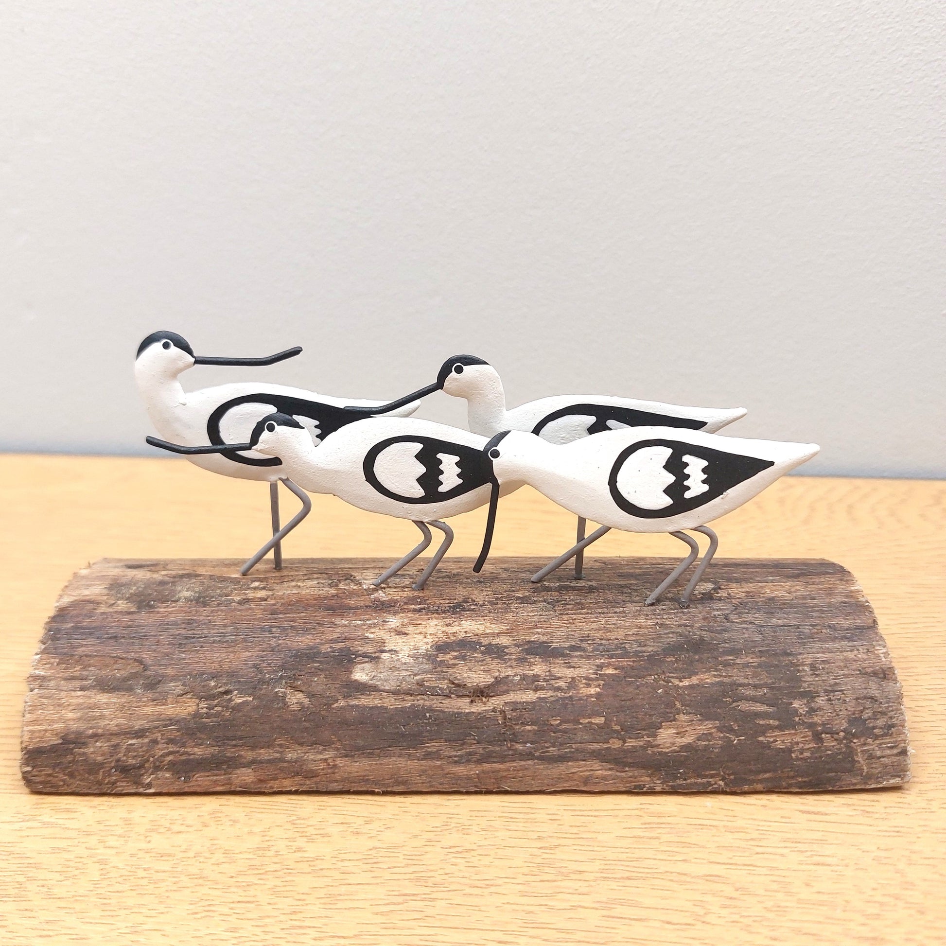 Decorative sculpture of four metal avocet birds on a wooden base against a light background