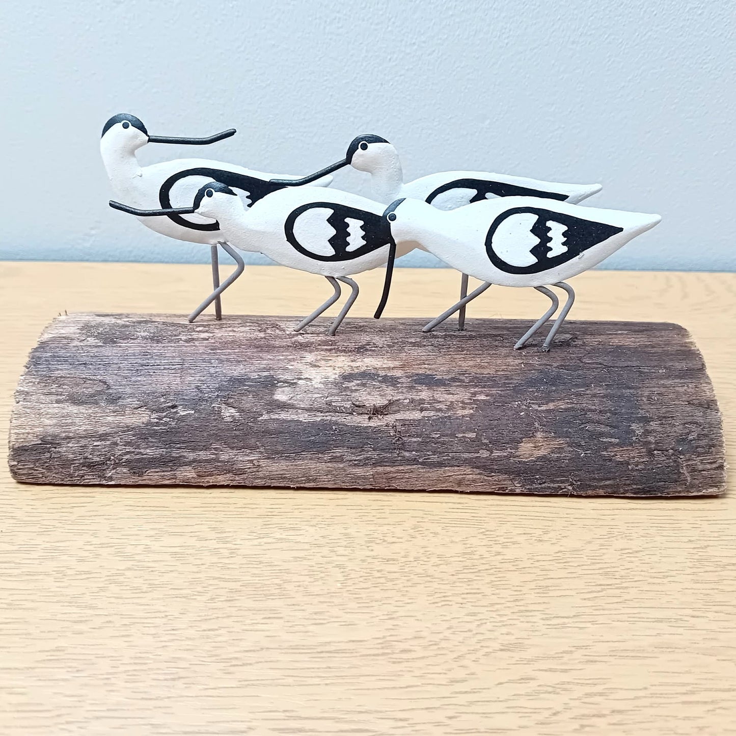 Decorative figurines of four black and white avocet birds on a wooden log against a light blue background