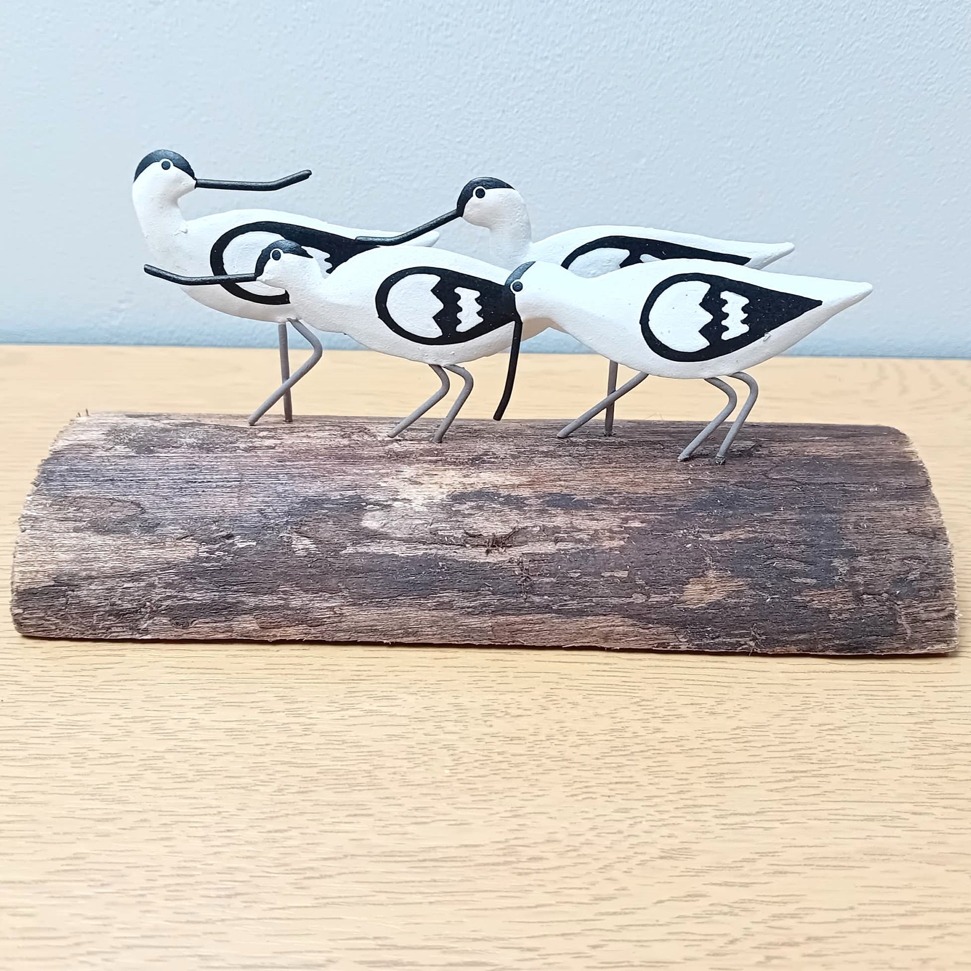 Decorative figurines of four black and white avocet birds on a wooden log against a light blue background