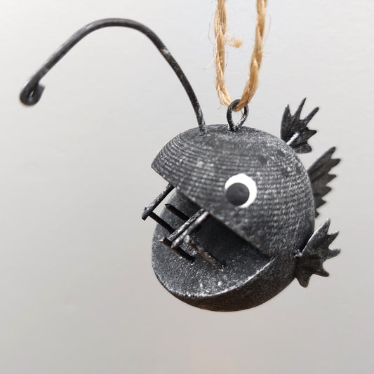 Decorative metal angler fish ornament on a plain background