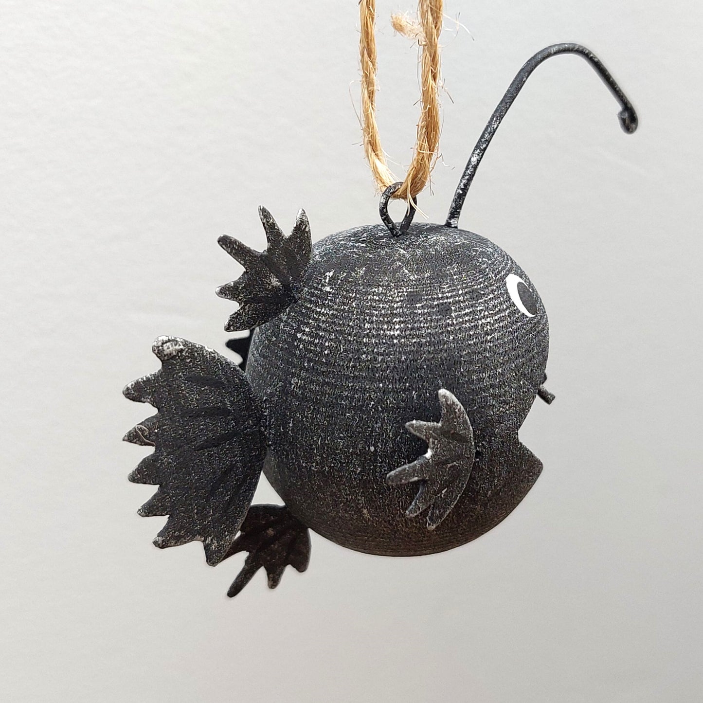 Black decorative ornament shaped like an angler fish on a white background