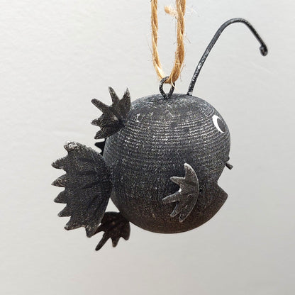 Black decorative ornament shaped like an angler fish on a white background