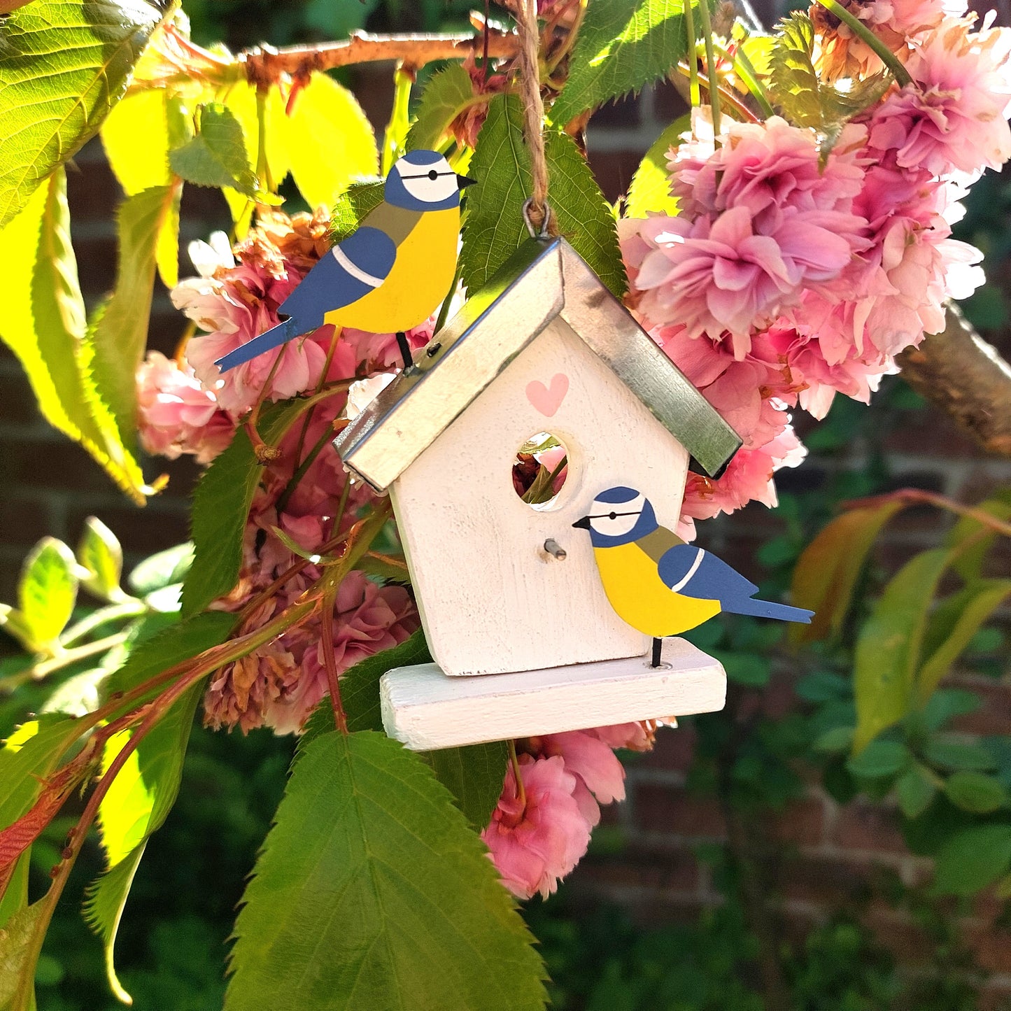 Decorative birdhouse with metal cute birds on a branch with pink flowers