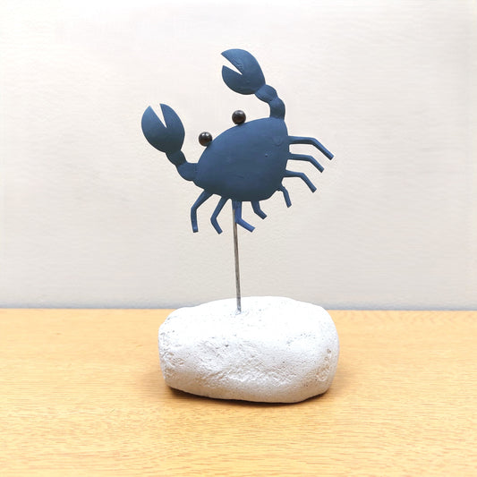 Blue crab-shaped figurine on a white rock against a light background