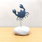 Blue crab-shaped figurine on a white rock against a light background