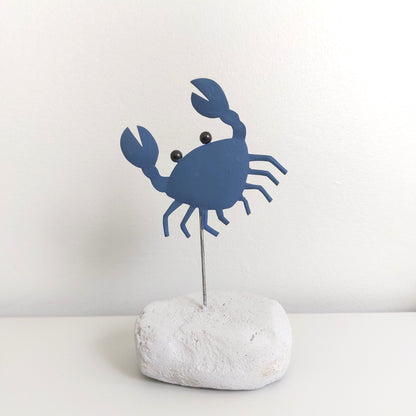 Blue crab-shaped decorative item on a white rock against a light gray background