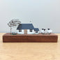 Ornamental wooden and metal scene of a windswept croft with a farmhouse, tree, sheep and stones on a wooden block against a grey background