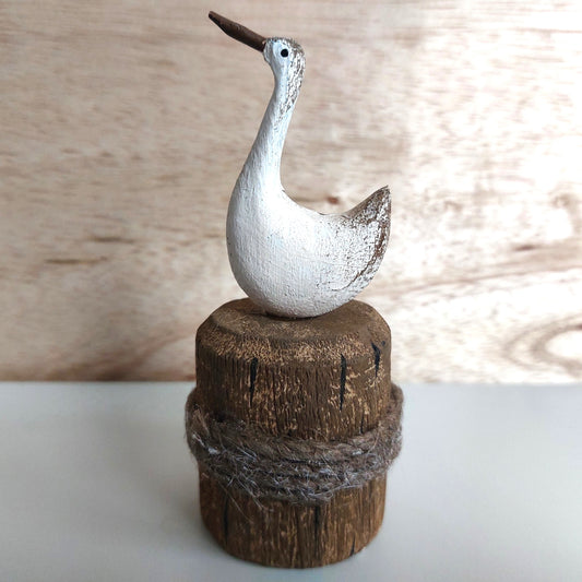 Decorative wooden and painted figurine of a bird on a wooden base with a natural background