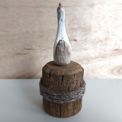 Decorative object with a textured white bird-like figure on a wooden base against a neutral background