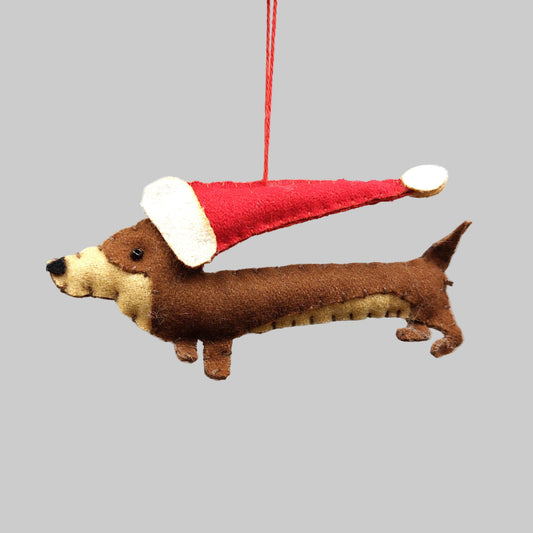 A brown felt sausage dog wearing a red Christmas hat, hanging from a red string against a white background