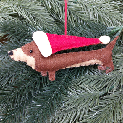 Dog-shaped felt Christmas ornament with a Santa hat on a green tree.