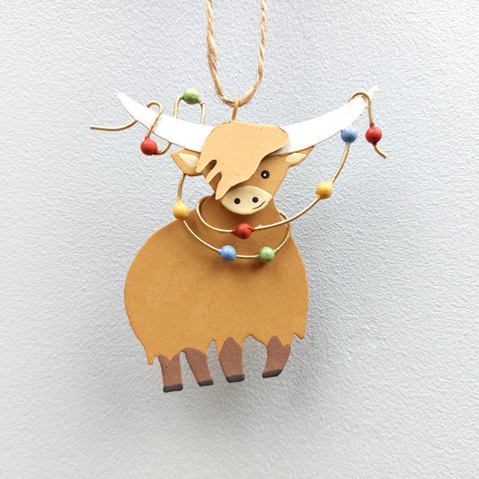 Decorative metal ornament shaped like a highland cow with colorful Christmas lights on a light gray background