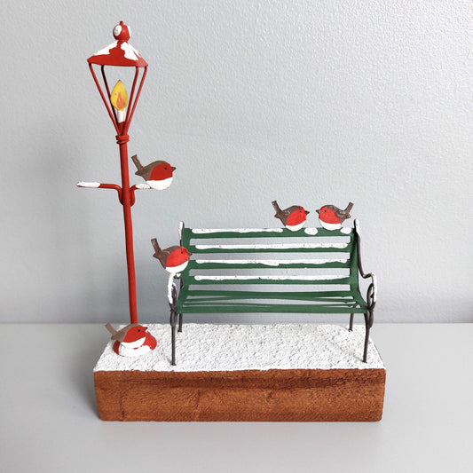 An ornamental scene of some robins on a park bench with a lamppost on a wooden block against a white background