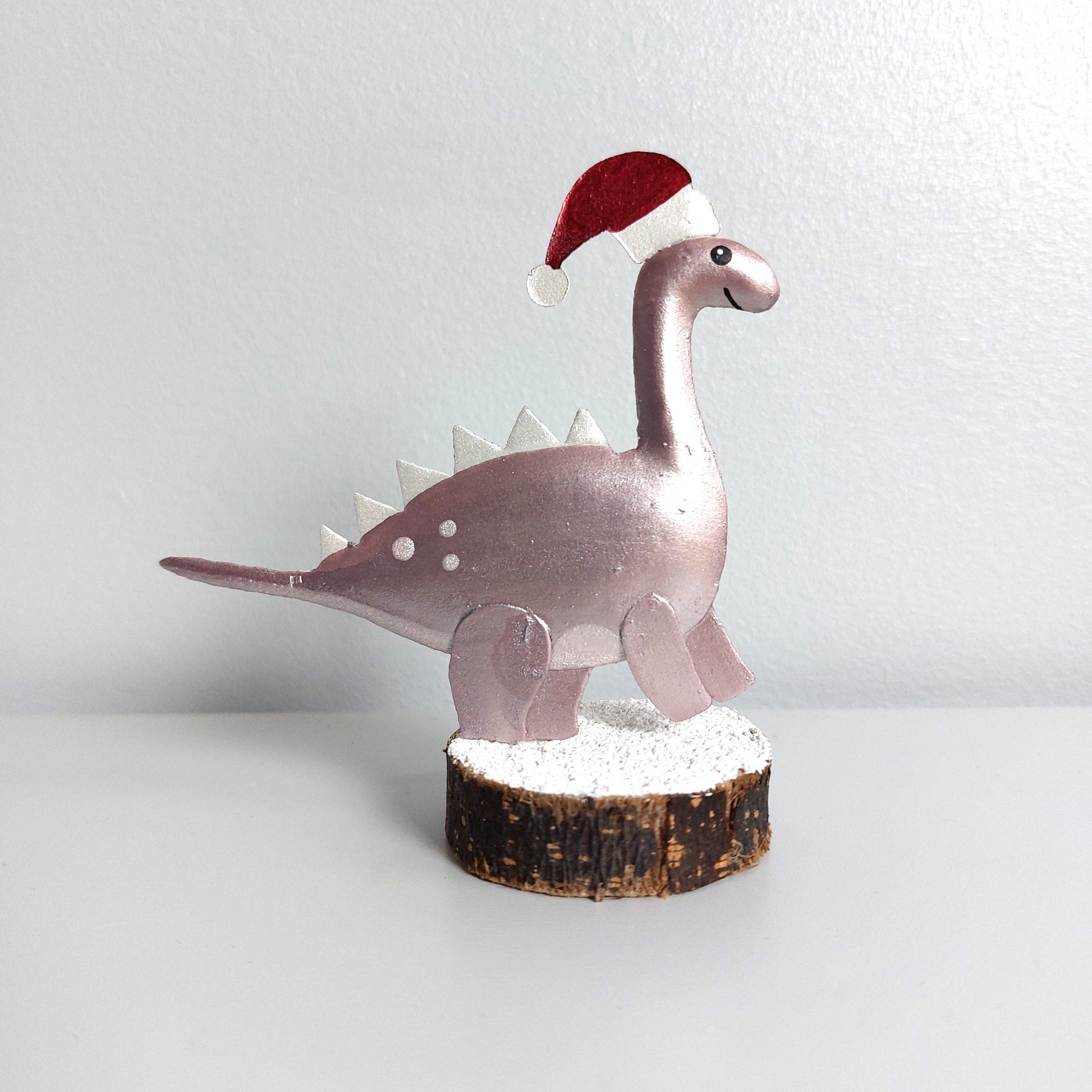 Decorative metal dinosaur figurine wearing a Santa hat on a white background