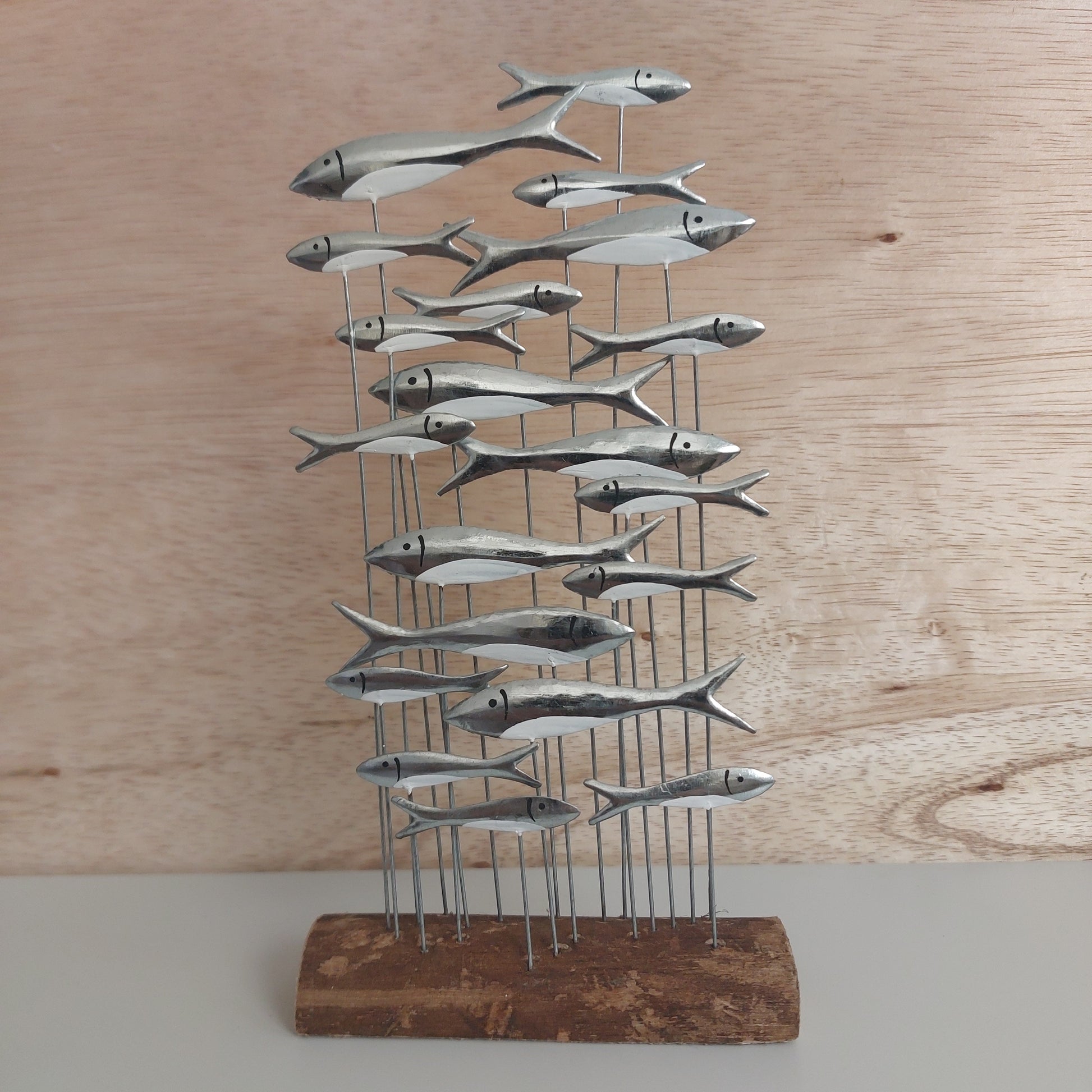 Metal fish wall art mounted on a wooden base against a wooden wall.