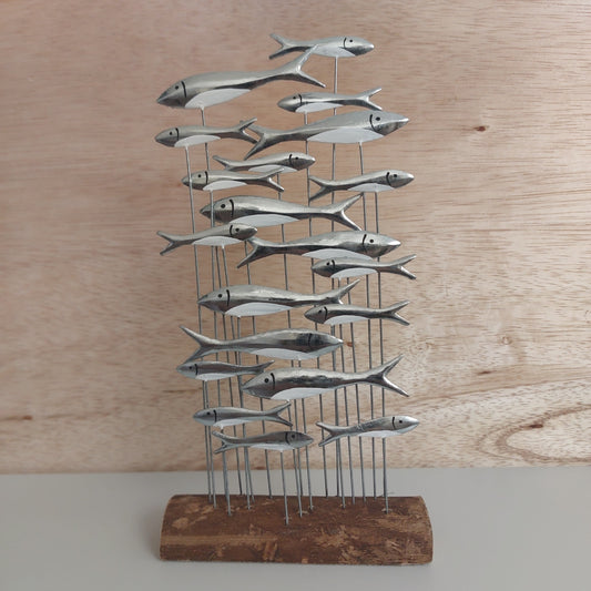 Metal fish wall art mounted on a wooden base against a wooden wall.