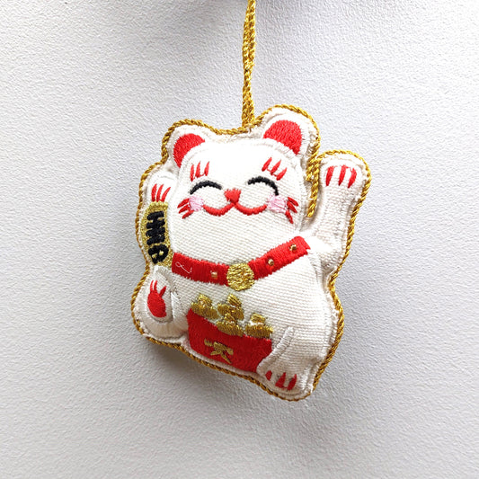 White cat-shaped fabric ornament with red and gold details on a white background