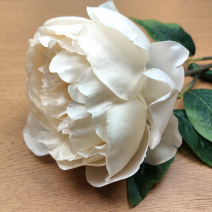 Artificial Ivory Peony flower with green leaves on a wooden surface