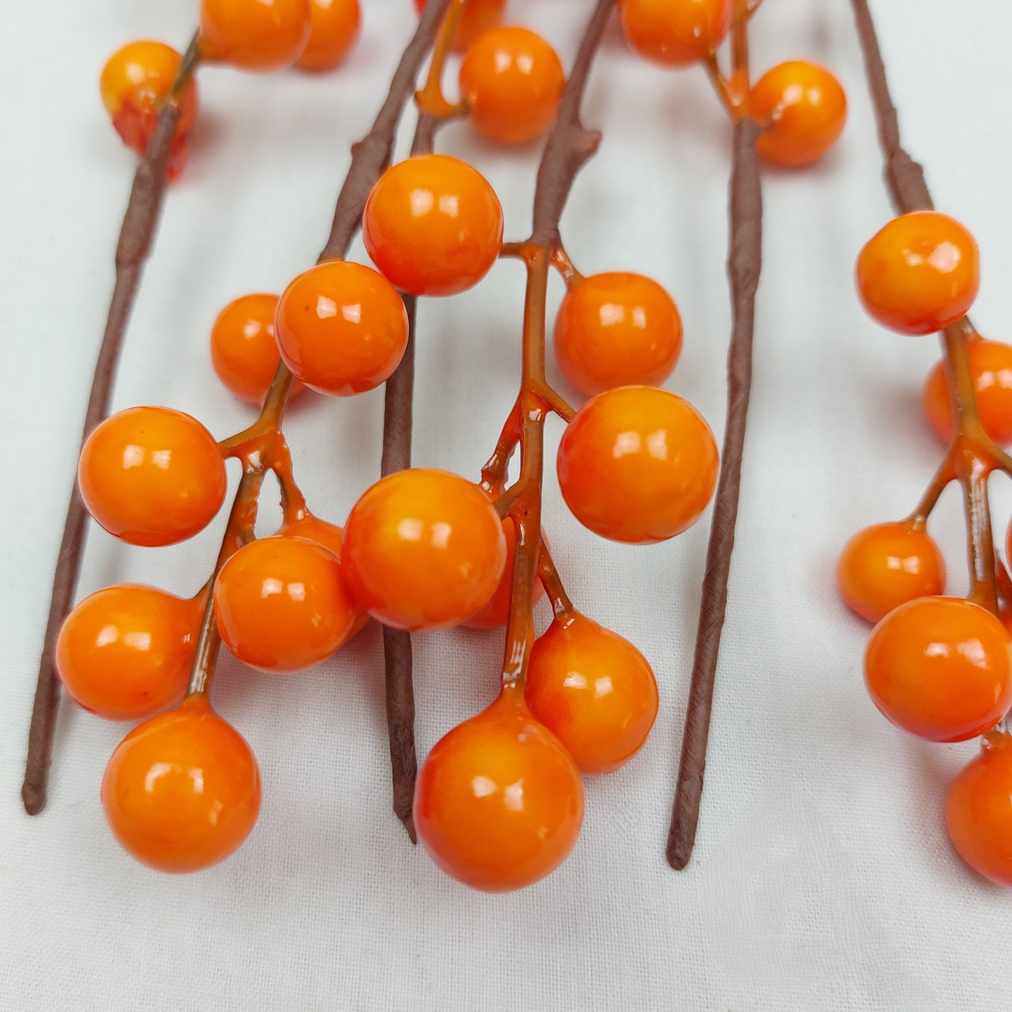 Close up of Artificial Orange berries on brown branches against a white background