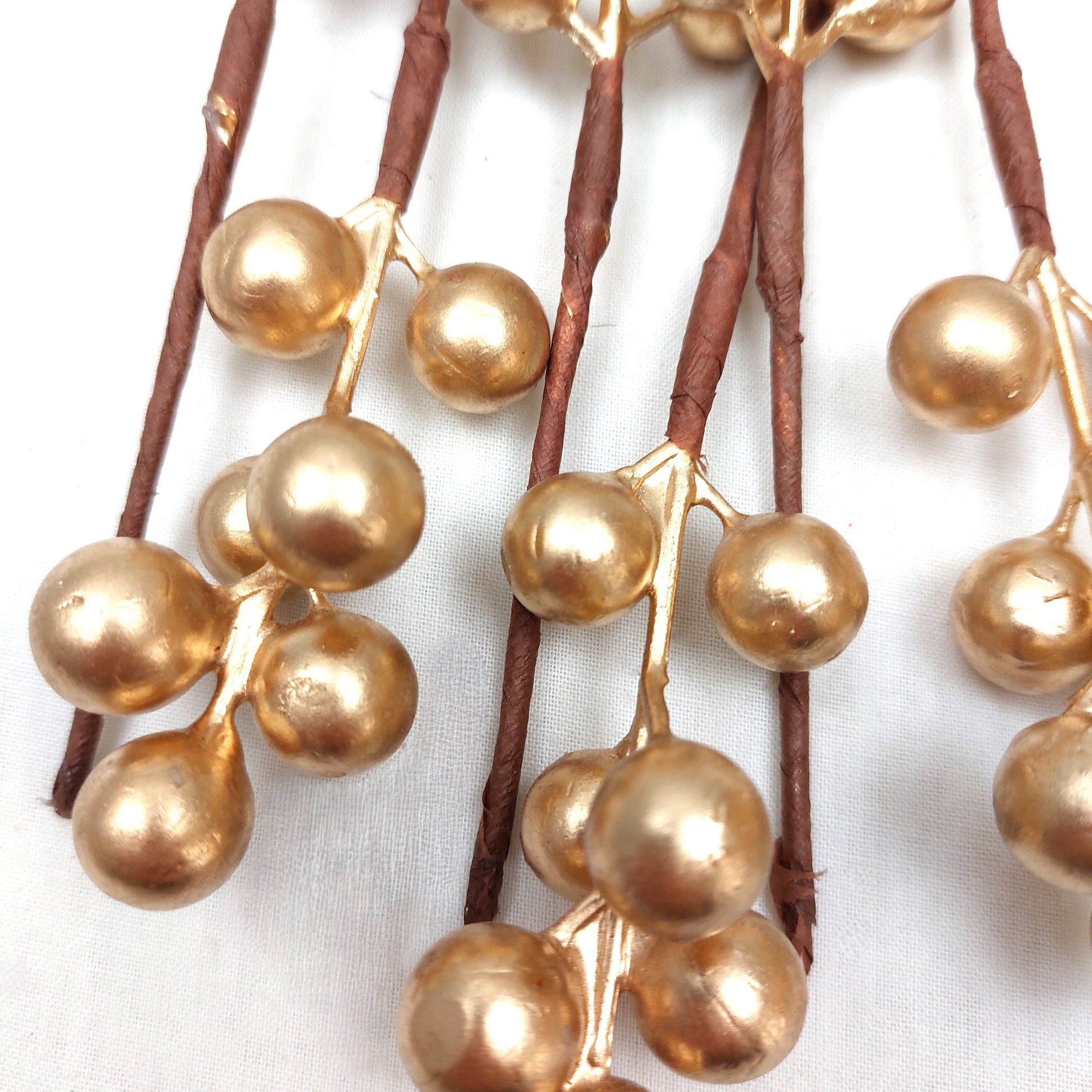 Close up of Gold berry decorations on brown stems against a white background
