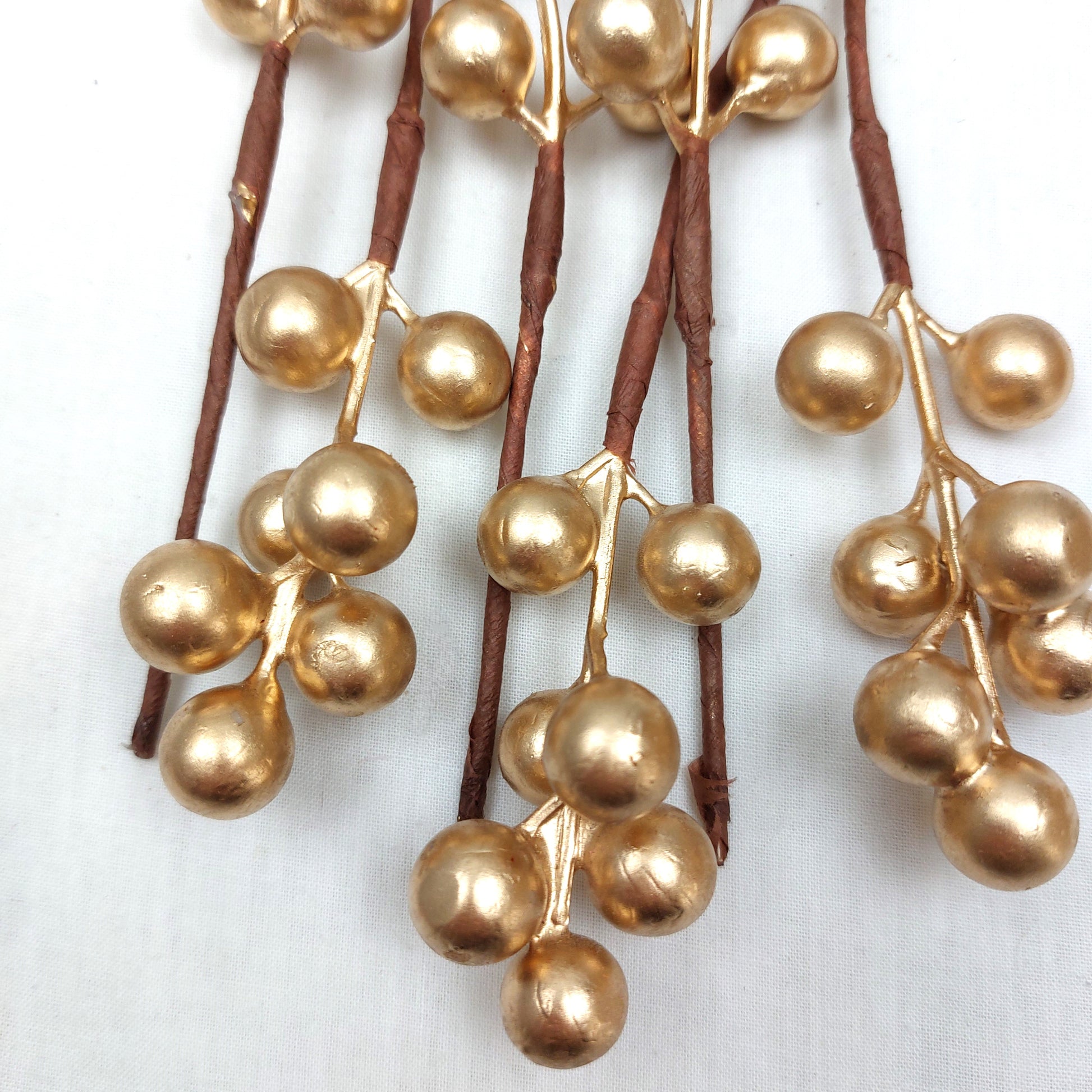Close up of Christmas Picks with gold berries on brown stems against a white background