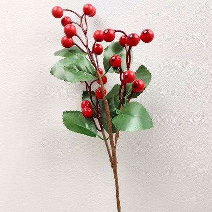Artificial red berry branch with green leaves on a light background