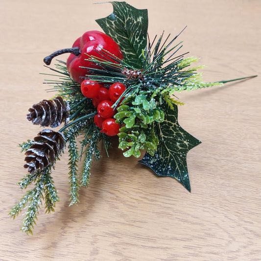 Decorative artificial Christmas arrangement with holly berries, pine cones, and greenery on a wooden surface.