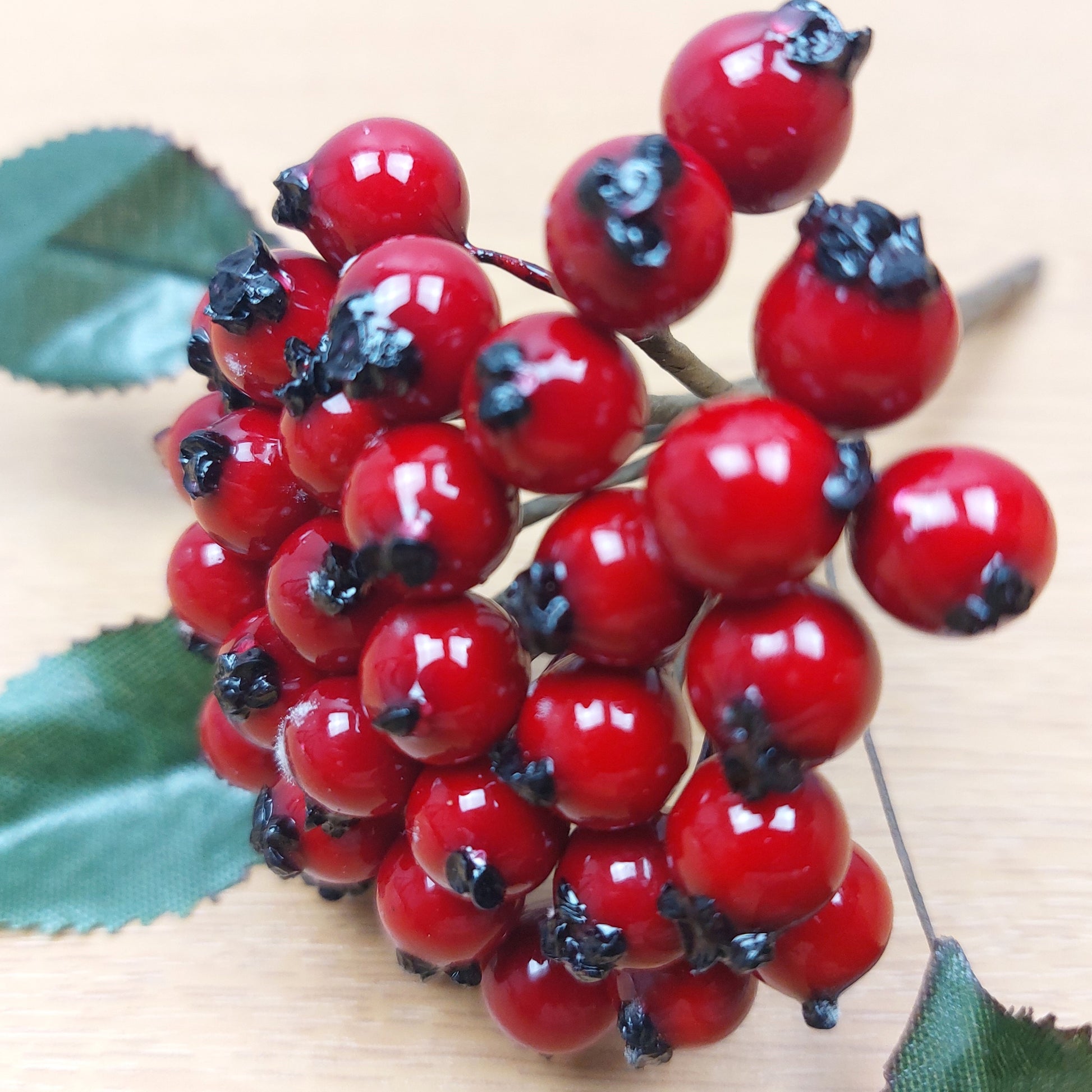 Close-up of artificial red berries with green leaves on a wooden surface