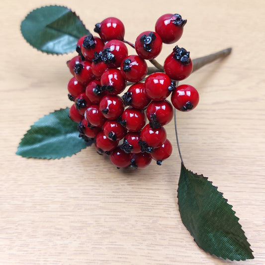 Artificial Red berry cluster with green leaves on a wooden background