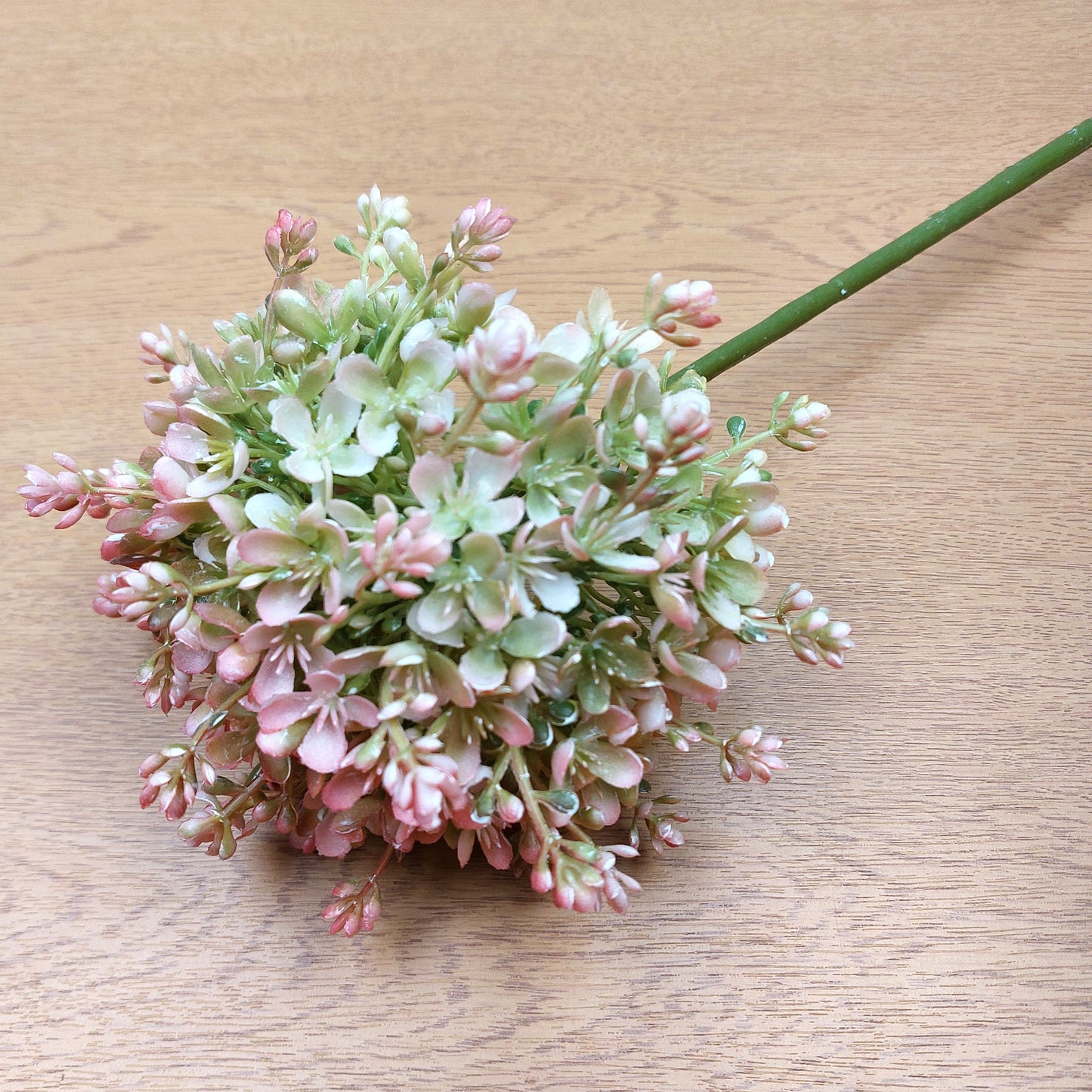 An artificial Pink and Green Allium Flower against a wooden background