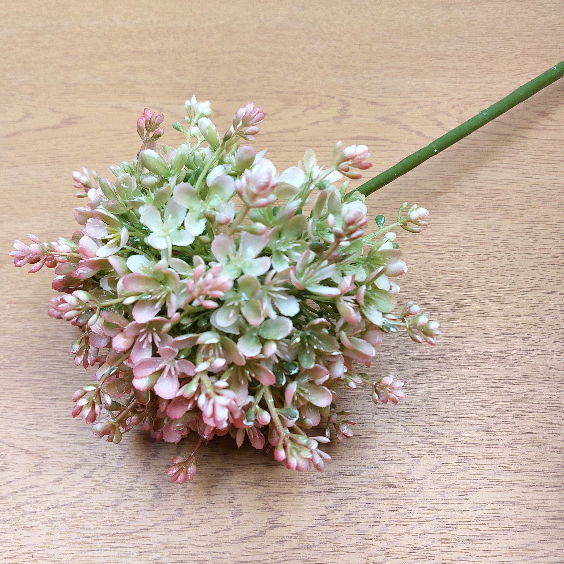 An artificial Pink and Green Allium Flower against a wooden background