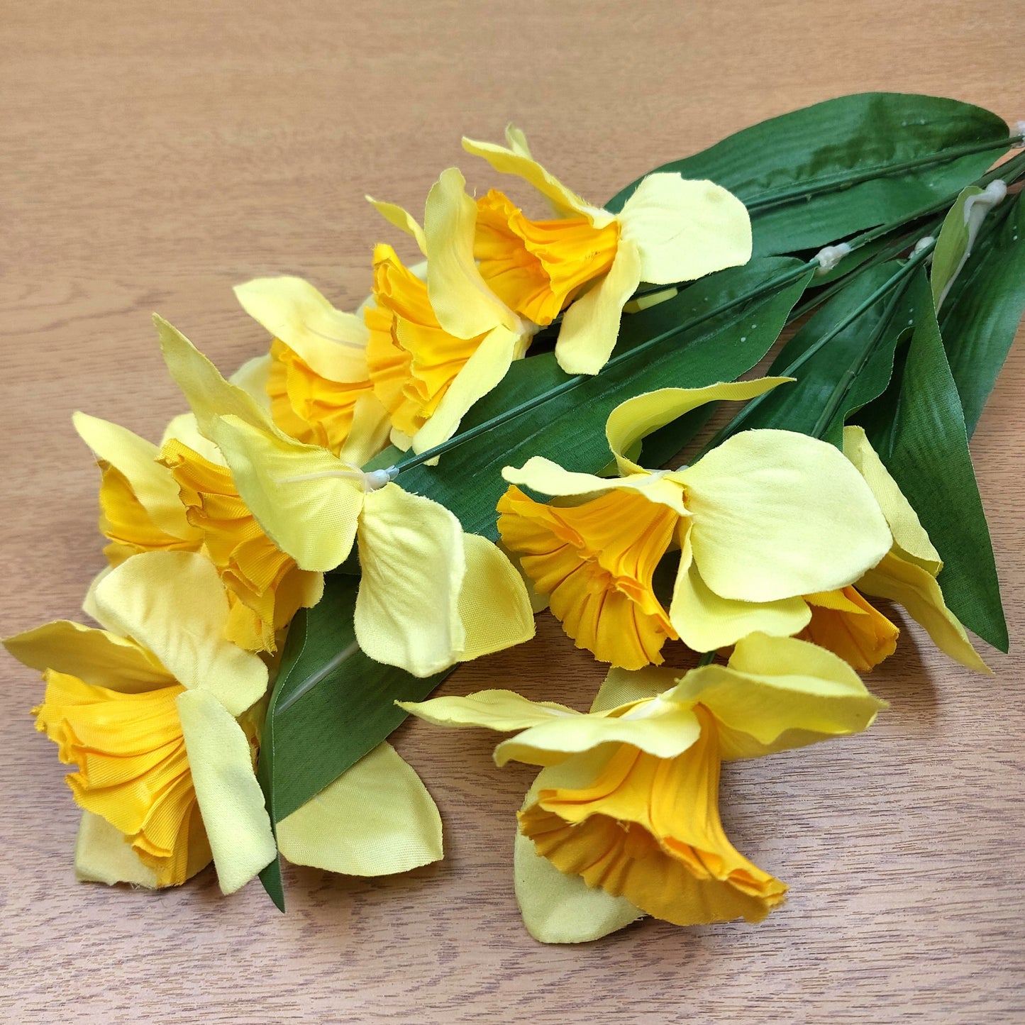A bunch of artificial Yellow Daffodils laying down on a wooden surface.