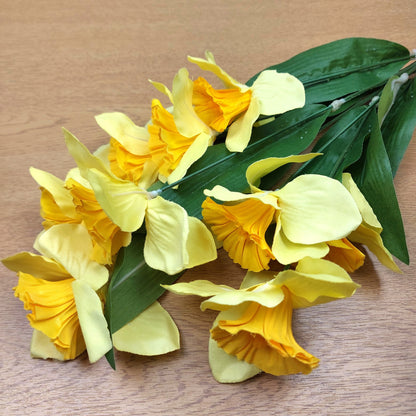 A bunch of artificial Yellow Daffodils laying down on a wooden surface.