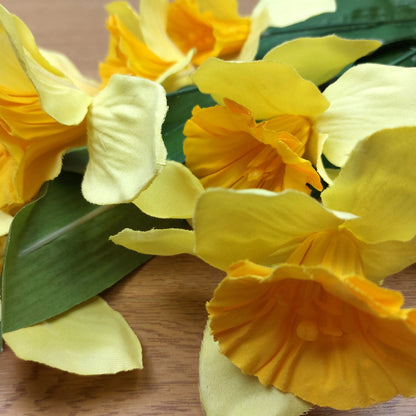 A close up of a bunch of artificial yellow Daffodils on a wooden surface.