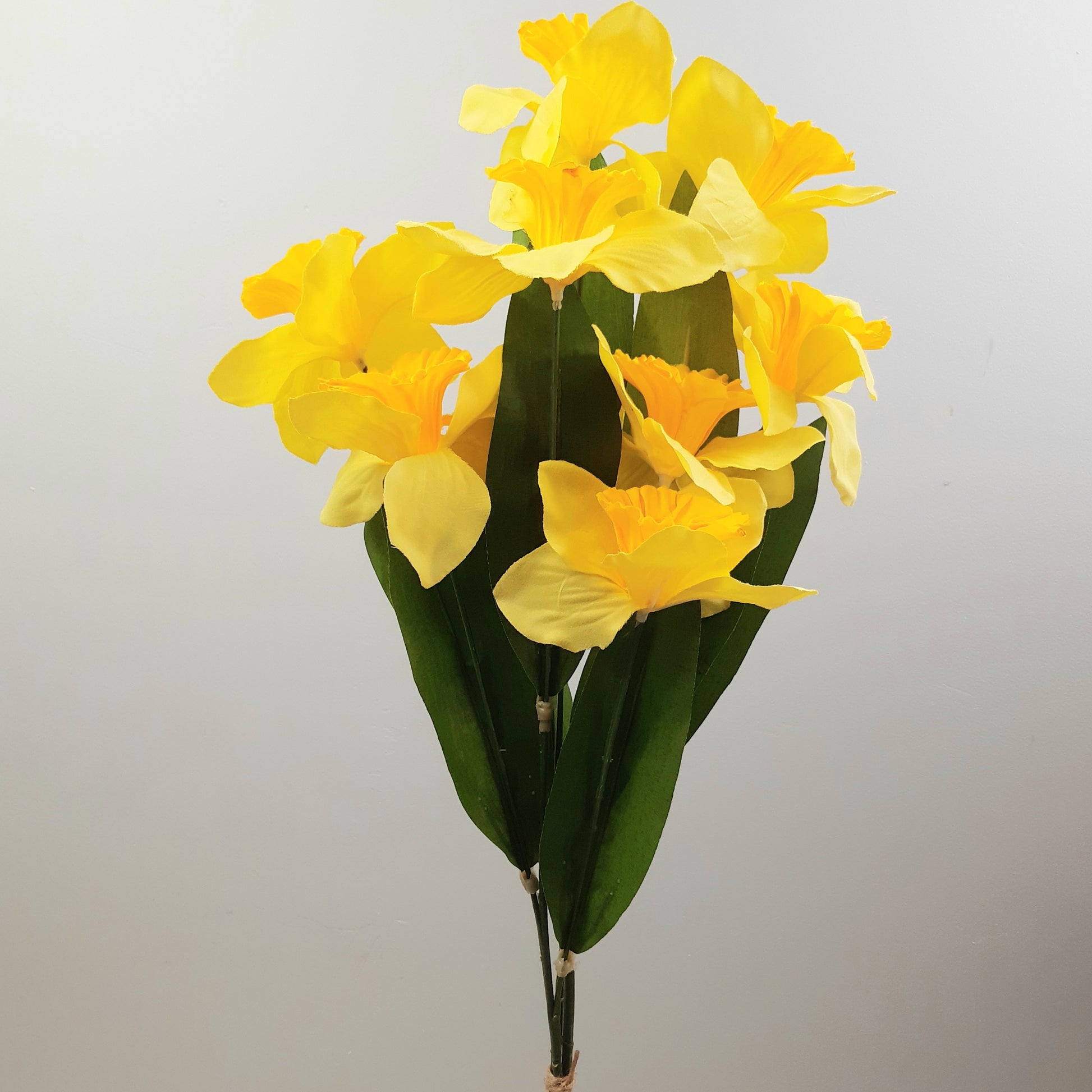 Artificial yellow daffodil spray with green leaves against a white background