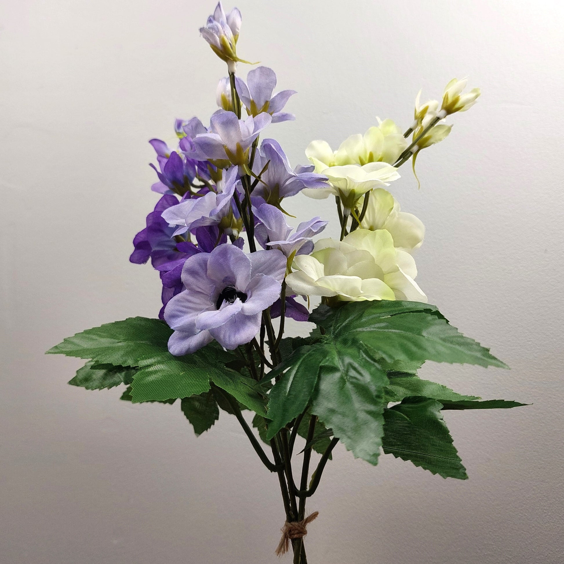 Bouquet of artificial purple and white Delphinium flowers with green leaves on a plain background