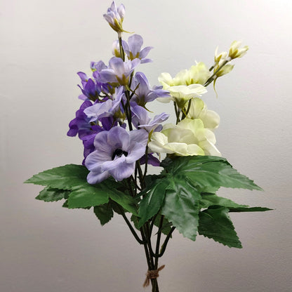 Bouquet of artificial purple and white Delphinium flowers with green leaves on a plain background