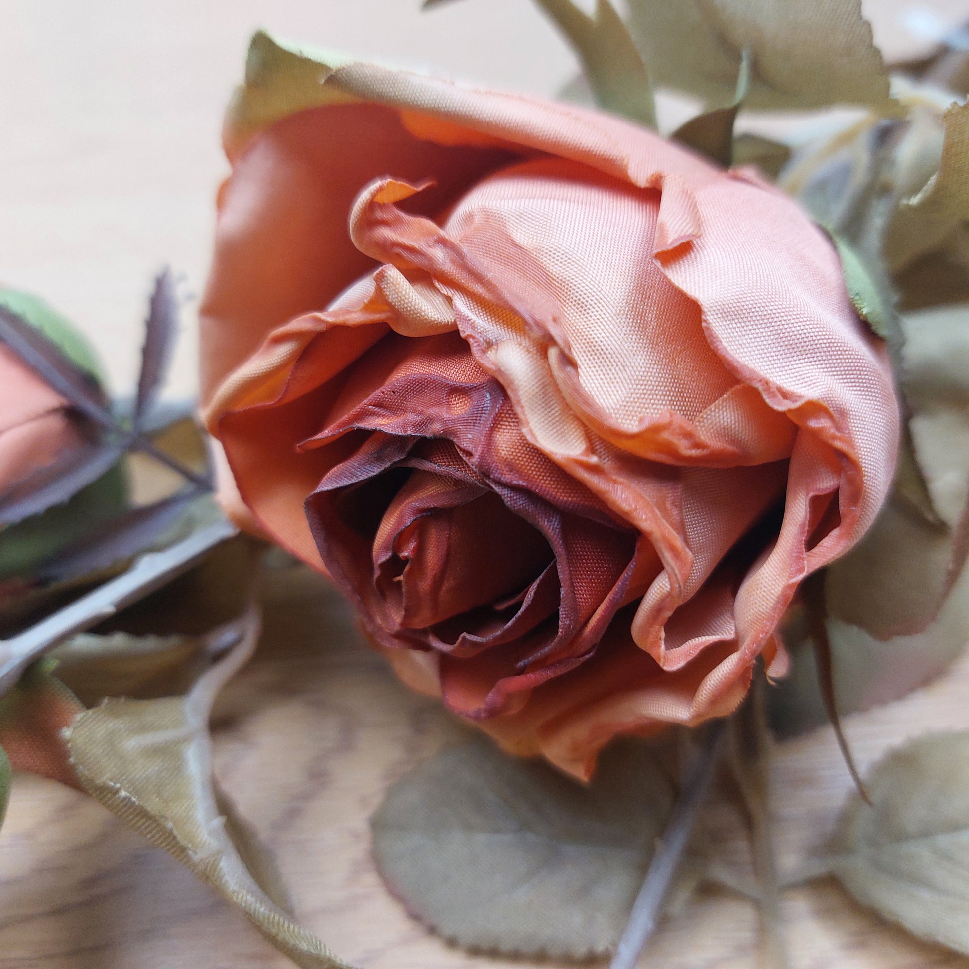 Close up of artificial orange cabbage rose head with green leaves.