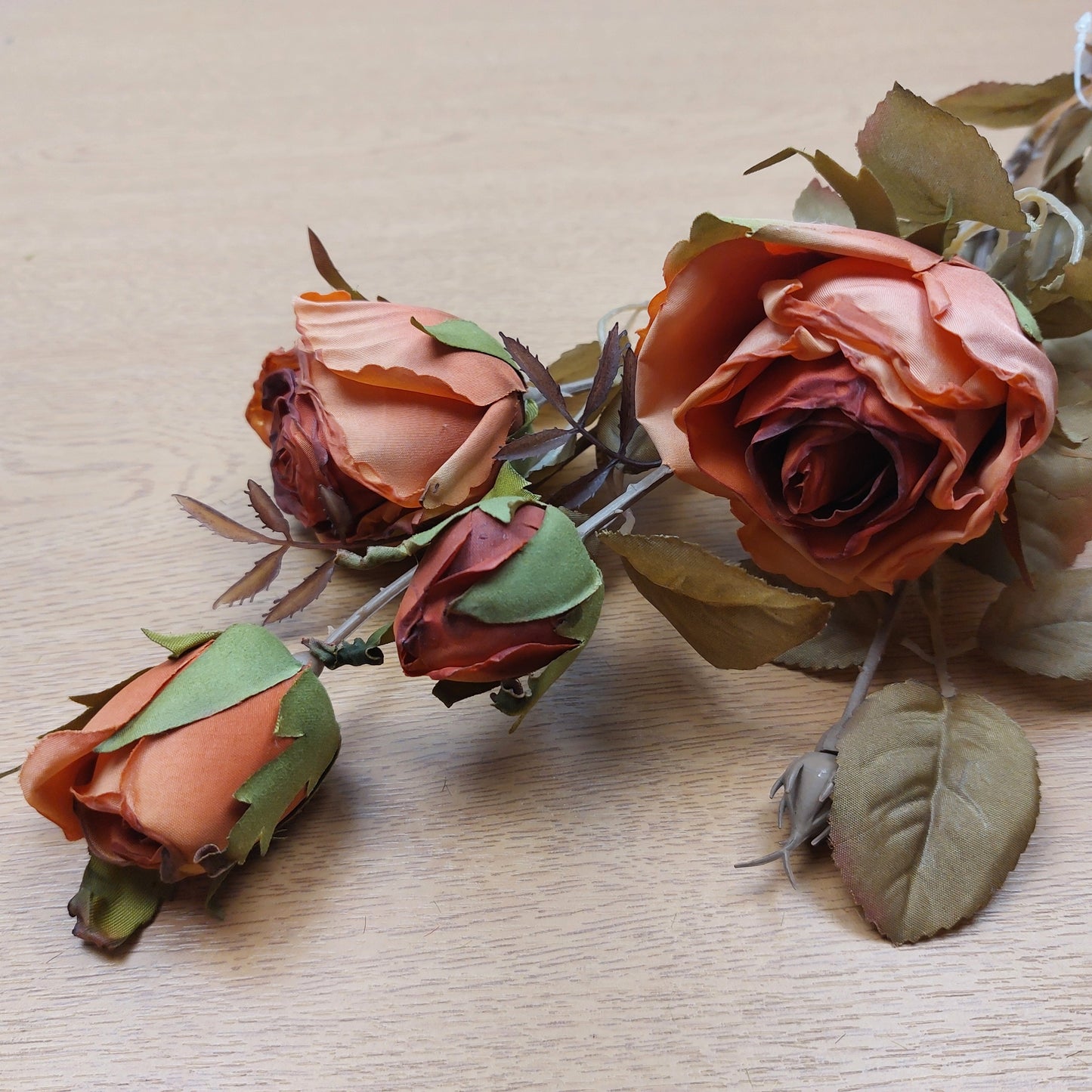 An artificial orange cabbage rose bunch laying down on a wooden background