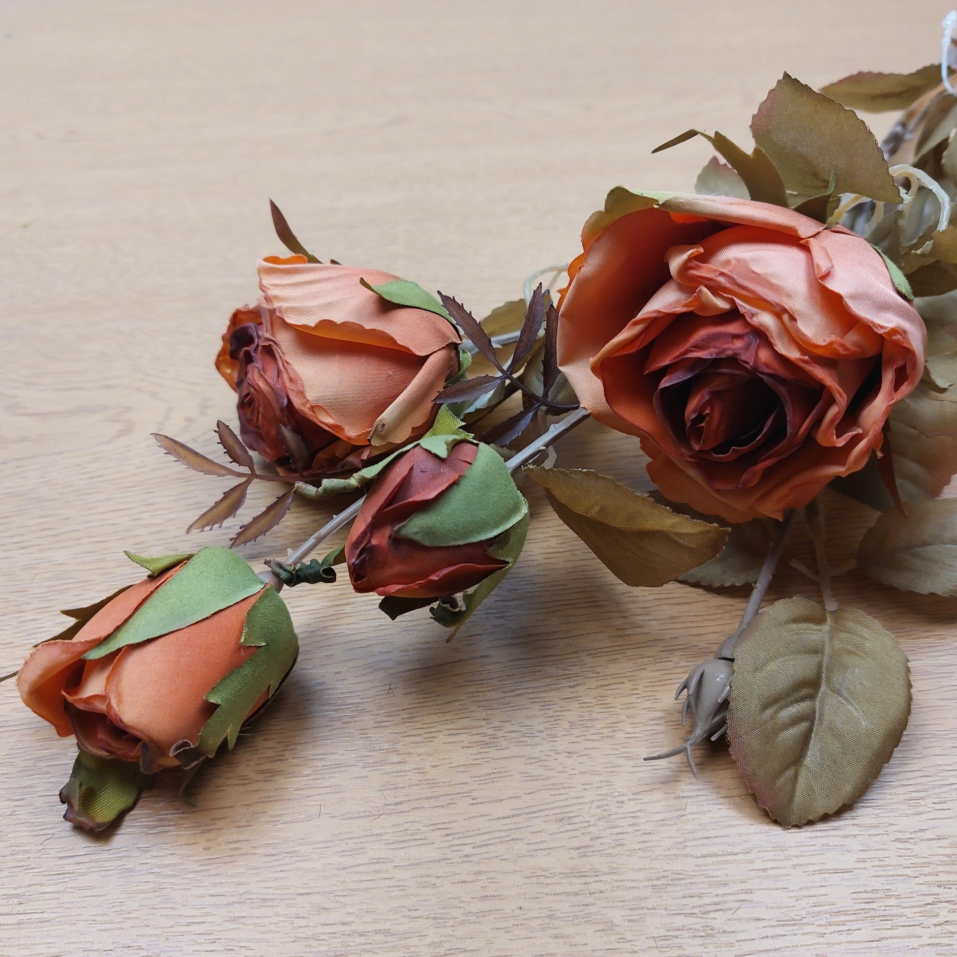 An artificial orange cabbage rose bunch laying down on a wooden background