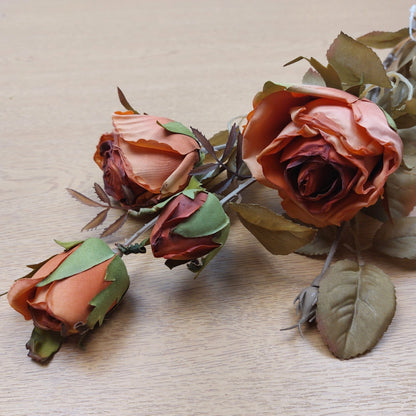An artificial orange cabbage rose bunch laying down on a wooden background