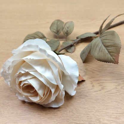Close up of a Cream artificial rose with green leaves on a wooden surface