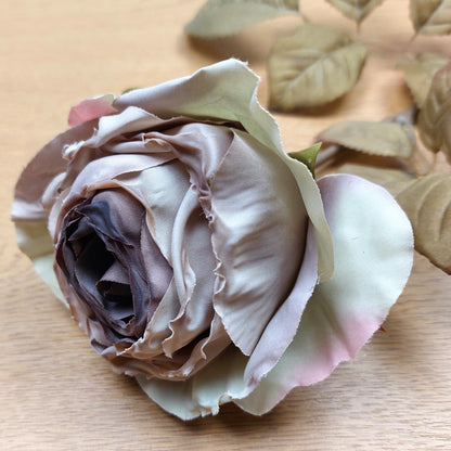 Close up of a Mauve artificial cabbage rose laying on a wooden background