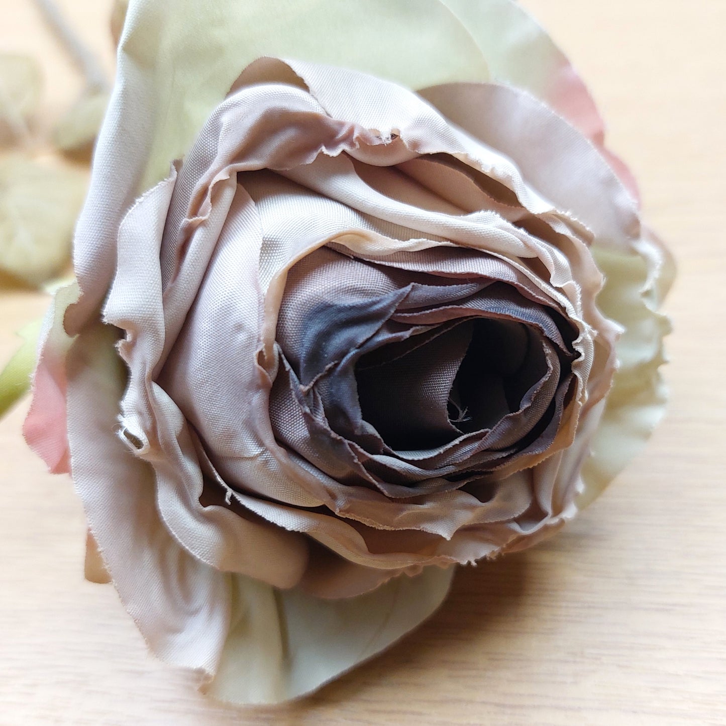 Close up of a dried look artificial mauve cabbage rose against a wooden background