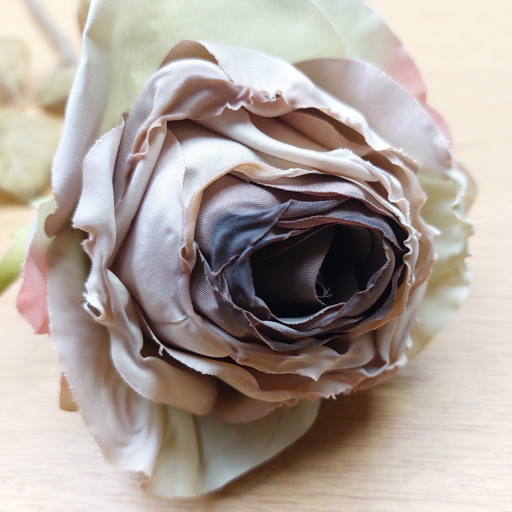Close up of a dried look artificial mauve cabbage rose against a wooden background